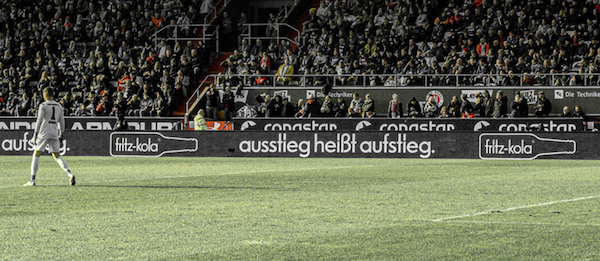 Spielfeldbegrenzung mit einem Banner der Firma Fritz-Kola. Auf dem Banner steht: Ausstieg heißt Aufstieg